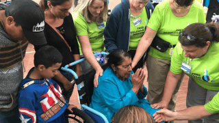 A number of caregivers praying with an Ecuadorian woman in a wheelchair.