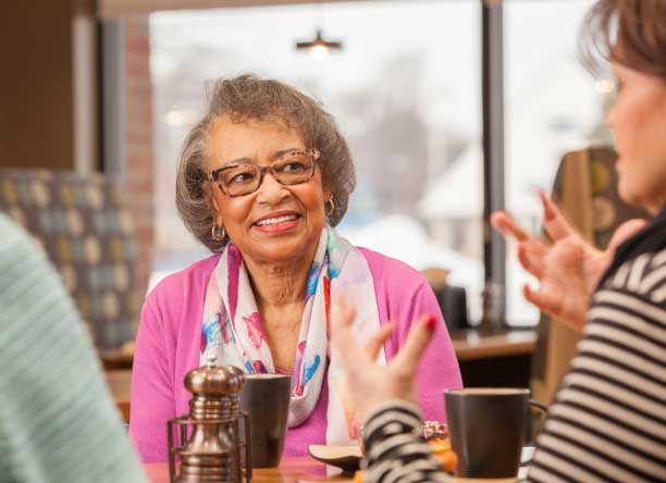 A client listening intently to her caregiver as they talk over coffee.