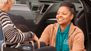 A female caregiver smiles up at her client as she prepares her wheelchair.