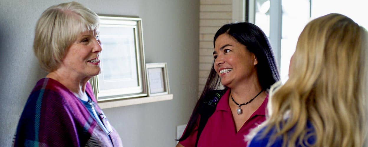 A caregiver in a mask looks at her client while talking to a family member.