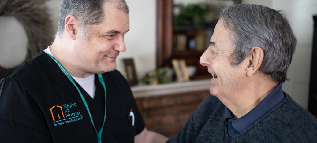 A caregiver smiles at his client, who laughs while telling a story.