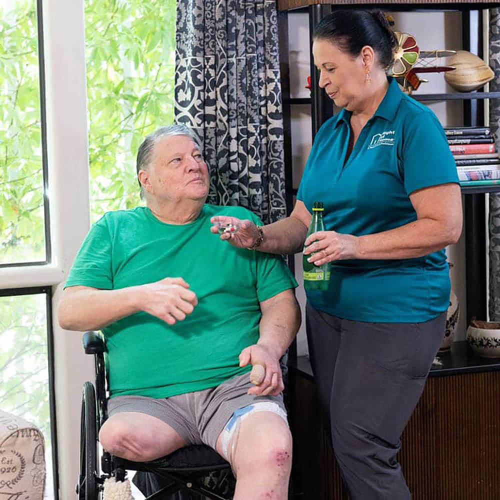 A female caregiver showing a bottle of pills to a female patient.