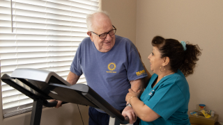 Female caregiver assisting elderly male patient on treadmill.